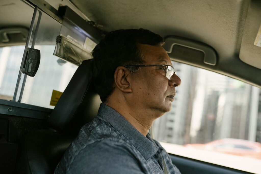 Side view of ethnic male in eyeglasses and casual clothes looking away while driving car
